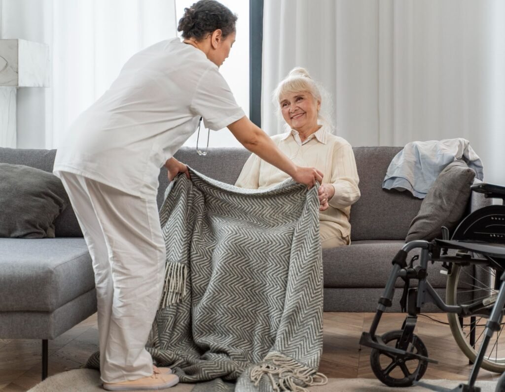 A nurse handing a blanket to senior woman at home